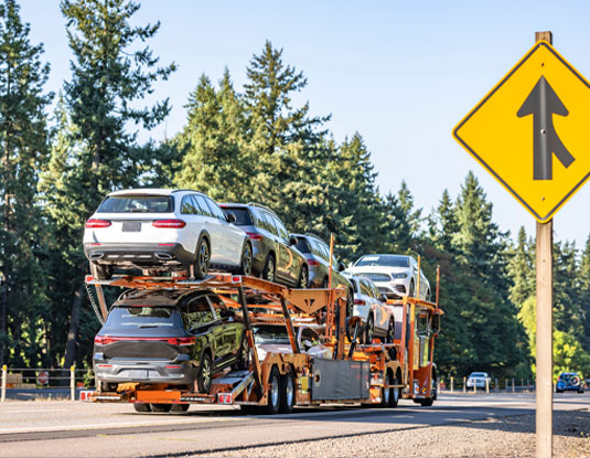 Bright orange classic car hauler with a two-level hydraulic trailer transporting vehicles on a divided highway, used for open auto transport services
