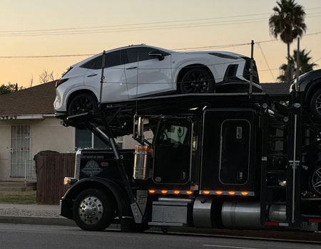 Open car carrier parked in front of a residential home, providing door-to-door car shipping services across the U.S.