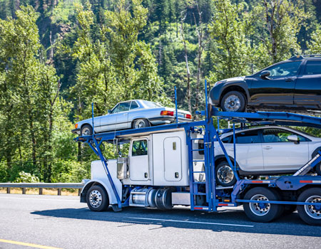 White car hauler semi-truck transporting vehicles on a two-level hydraulic trailer along a one-way highway, performing cross-country auto transport services