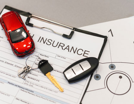 Car insurance paperwork with keys and a diecast model on a table, representing coverage included in auto transport services