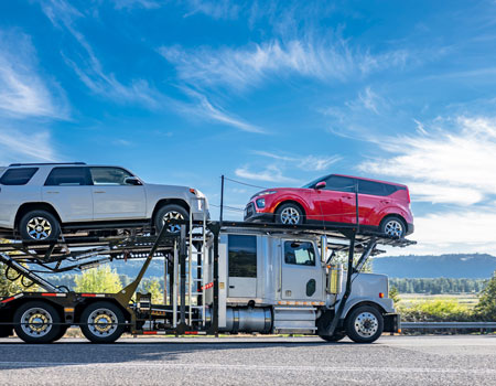 White big rig open car hauler transporting vehicles on a winding road, providing expedited car transport services through diverse terrain