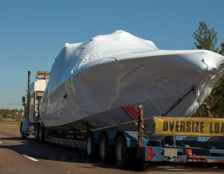 Oversized boat loaded on a specialized trailer for highway transport, handled by experienced boat shipping professionals