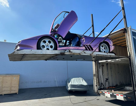 Exotic car being loaded into an enclosed trailer using a lift gate, highlighting secure exotic car shipping services